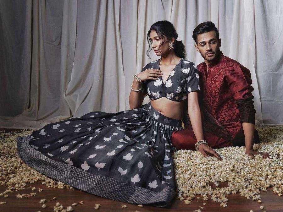 Two influencers styled by Tanya Jain seated together on a floor of white petals, in a monochrome floral lehenga and a red kurta